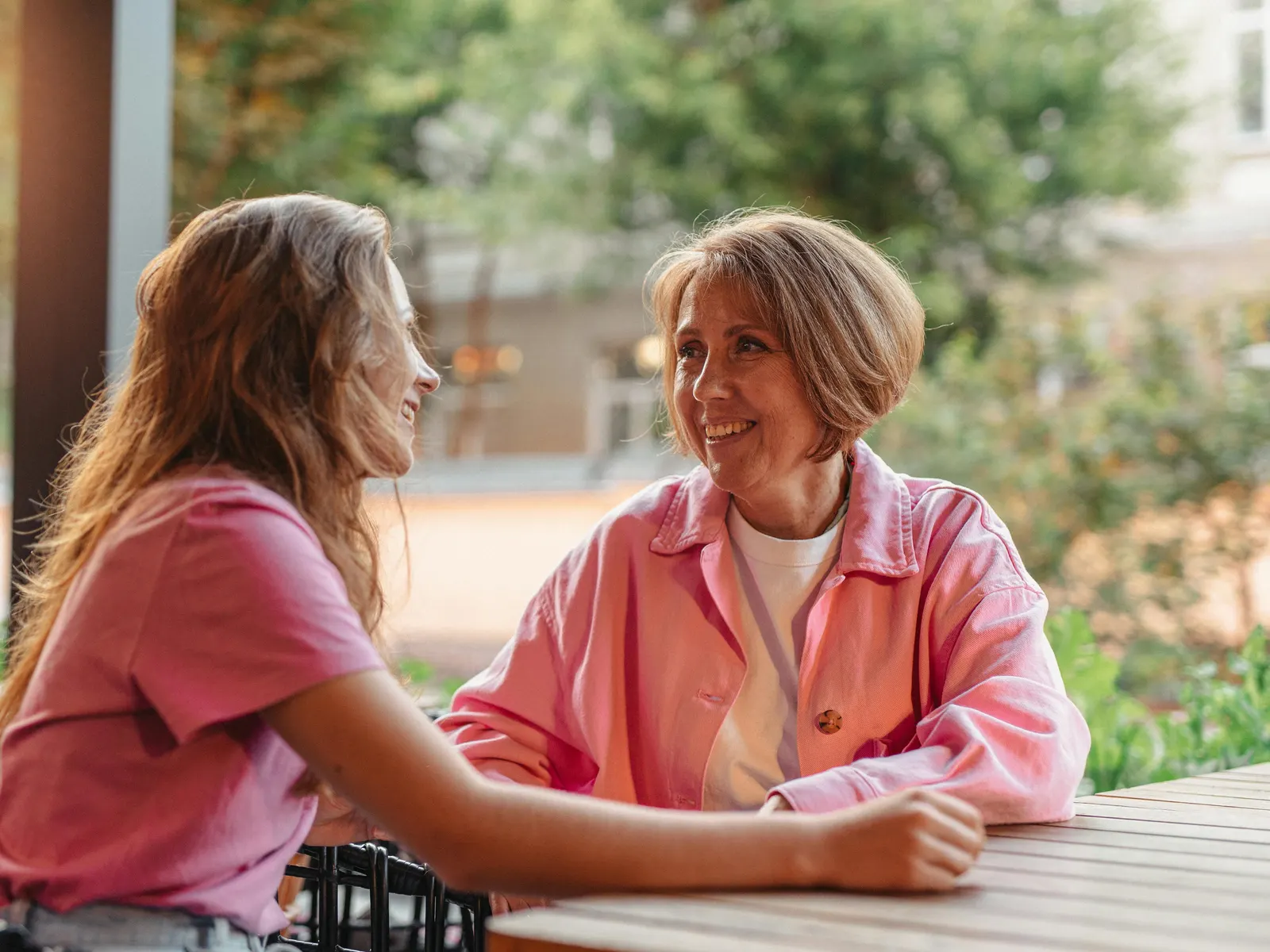 A mother and her adult daughter laughing together at a café table.